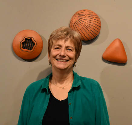 Photograph of Claudia Poser ceramic artist in front of one of her ceramic wall sculpture installations