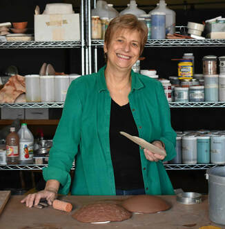 Photo of Claudia Poser ceramic artist in her studio hand building a terra cotta pod 