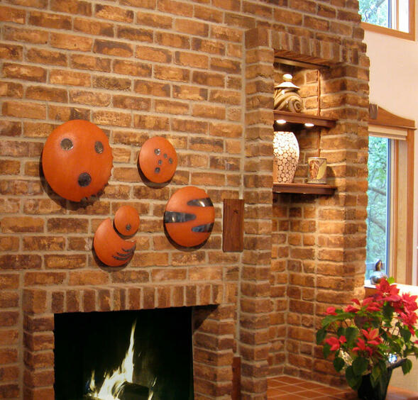 Ceramic wall sculpture installation above a fireplace of large terra cotta pods resembling planets with metallic accents