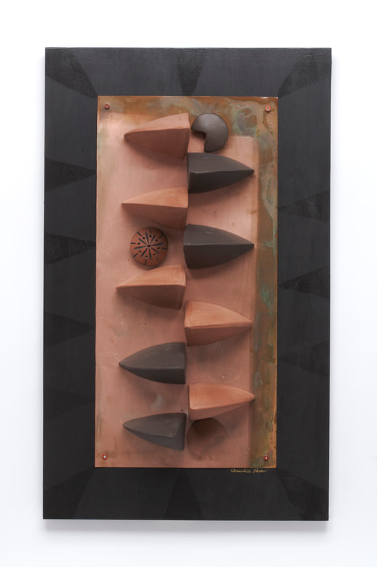 Post-modern wall piece composed of red and black terra cotta elements installed on a weathered copper sheet framed in black
