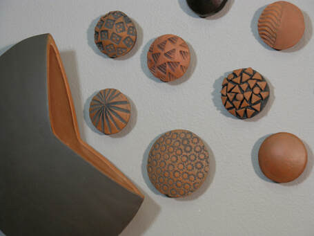 Detail of a ceramic wall sculpture installation containing round textured  terra cotta elements 