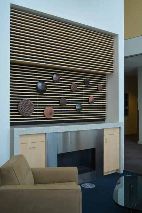 Abstract ceramic wall sculpture installation above a fireplace consisting of textured round terra cotta pods in black and terra cotta