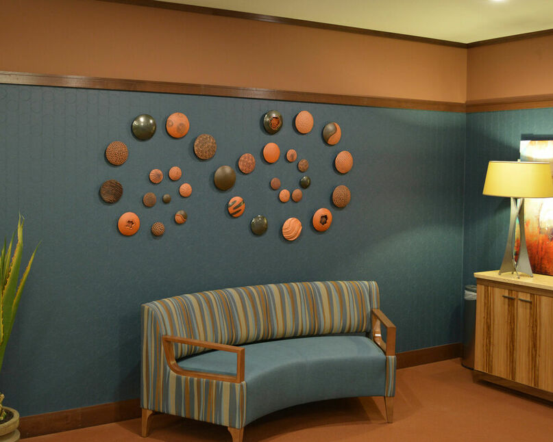  Abstract ceramic wall sculpture installation in a waiting area consisting of round textured terra cotta pods in black and terra cotta installed in spirals